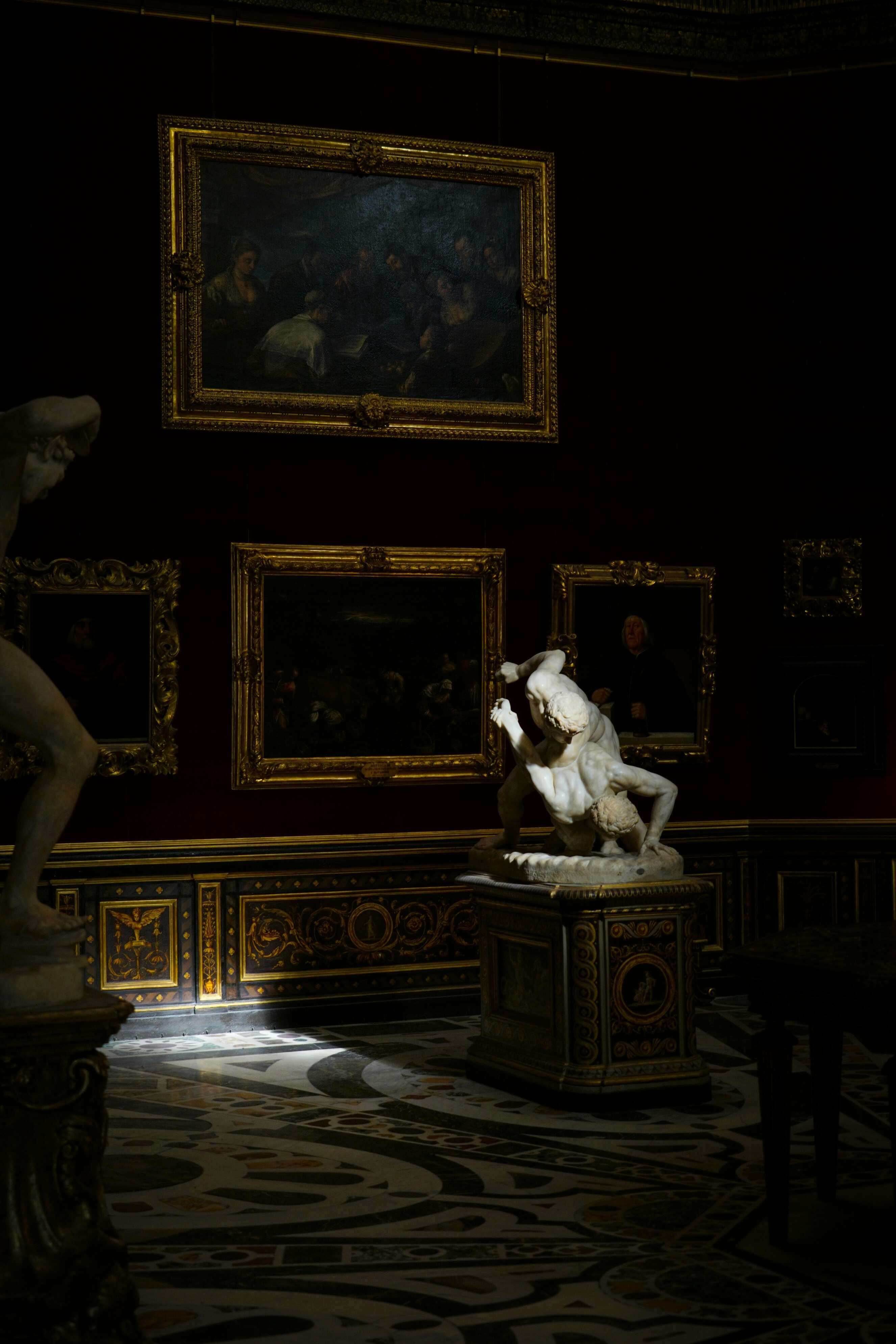 Marble wrestlers statue in a dark gallery of gilded paintings